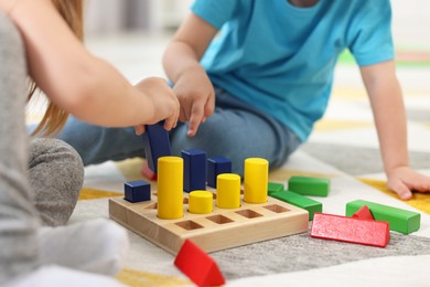 Photo of Little children playing with set of wooden geometric figures on carpet, closeup. Kindergarten activities for motor skills development