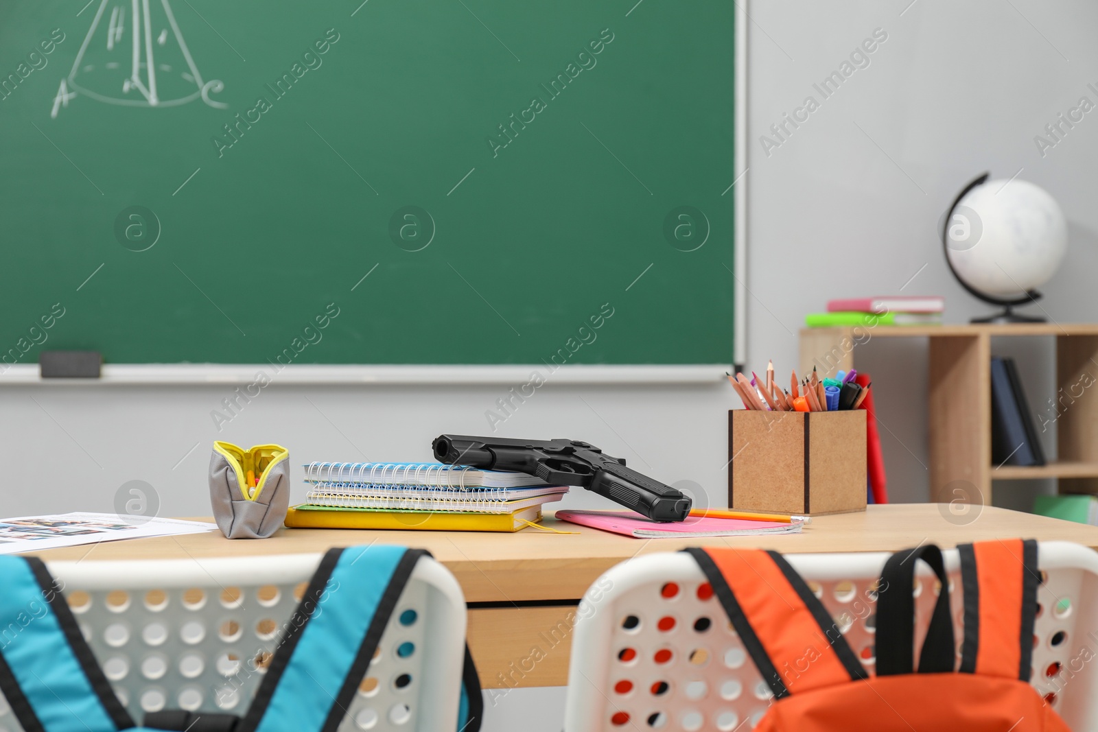 Photo of School stationery and gun on desk in classroom