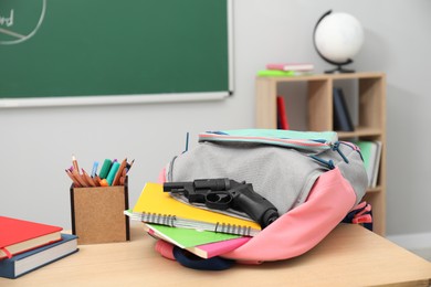 Photo of School stationery, gun and backpack on desk in classroom