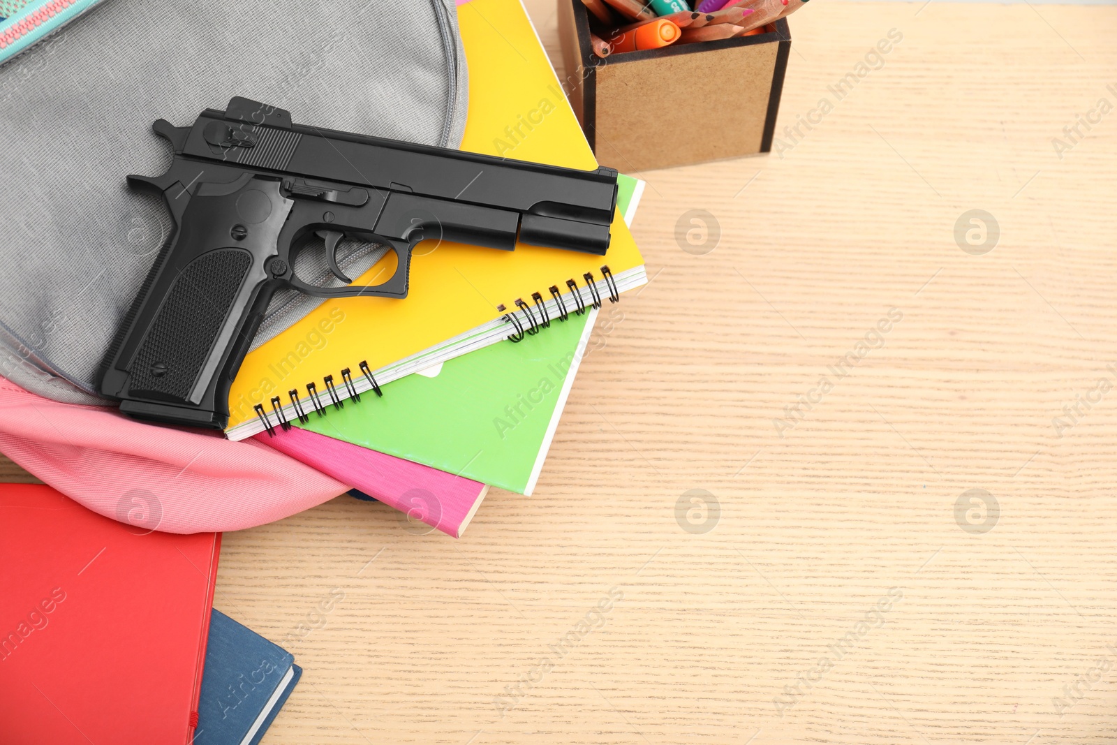 Photo of School stationery, gun and backpack on wooden desk, above view. Space for text
