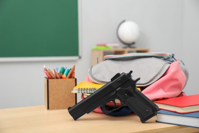 Photo of School stationery, gun and backpack on desk in classroom