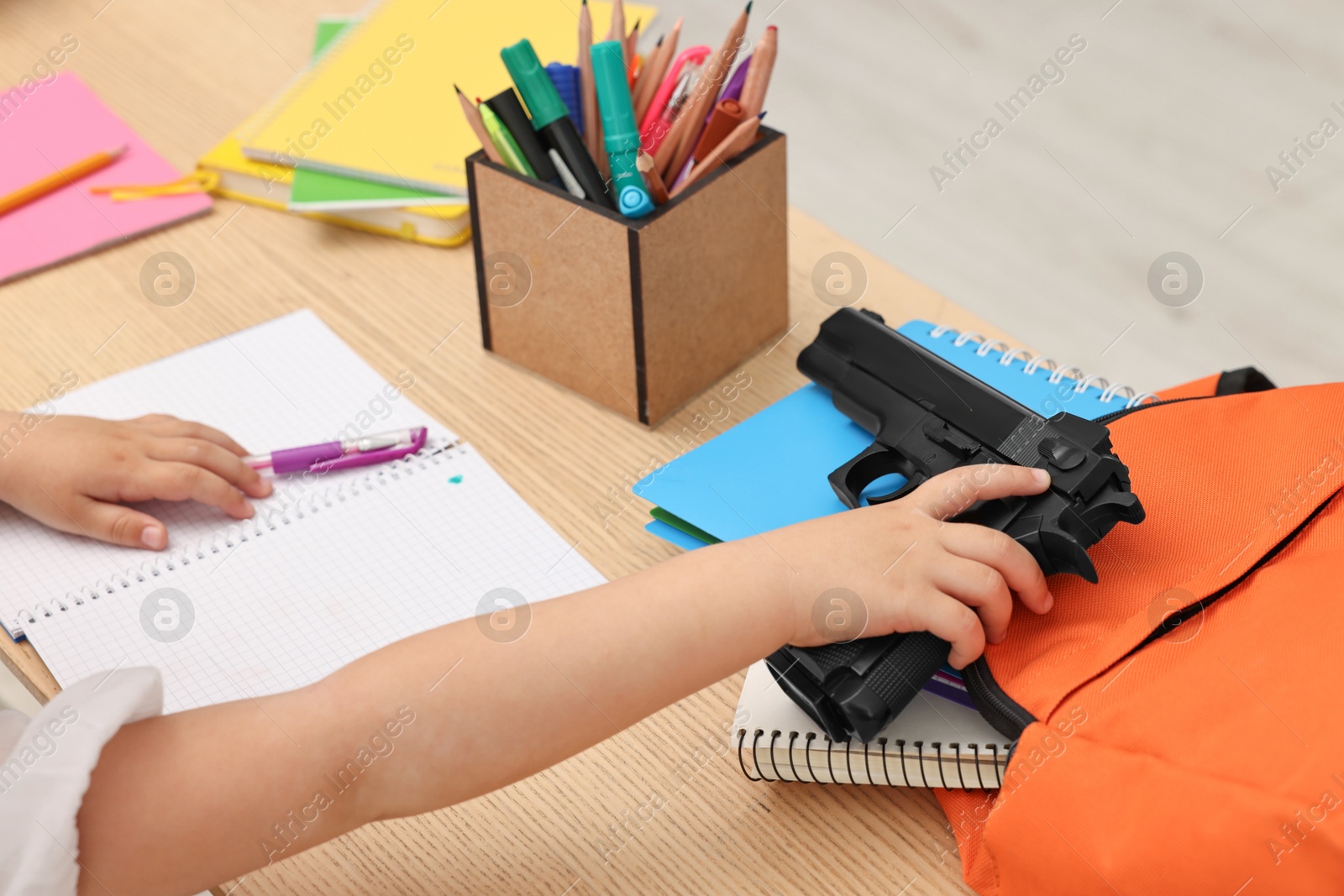 Photo of Child with gun and school stationery at desk in classroom, closeup