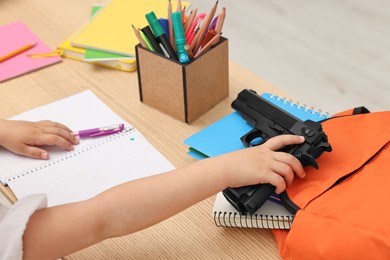 Child with gun and school stationery at desk in classroom, closeup