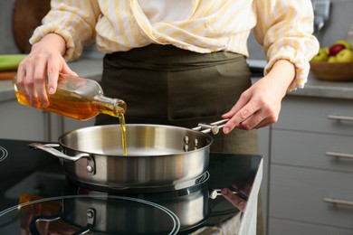 Photo of Vegetable fats. Woman pouring oil into frying pan on cooktop in kitchen, closeup