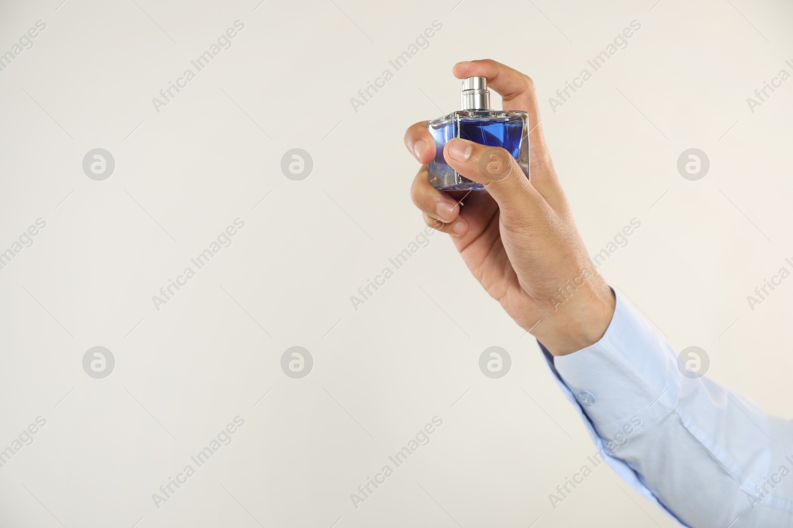 Photo of Man spraying luxury perfume on light background, closeup. Space for text