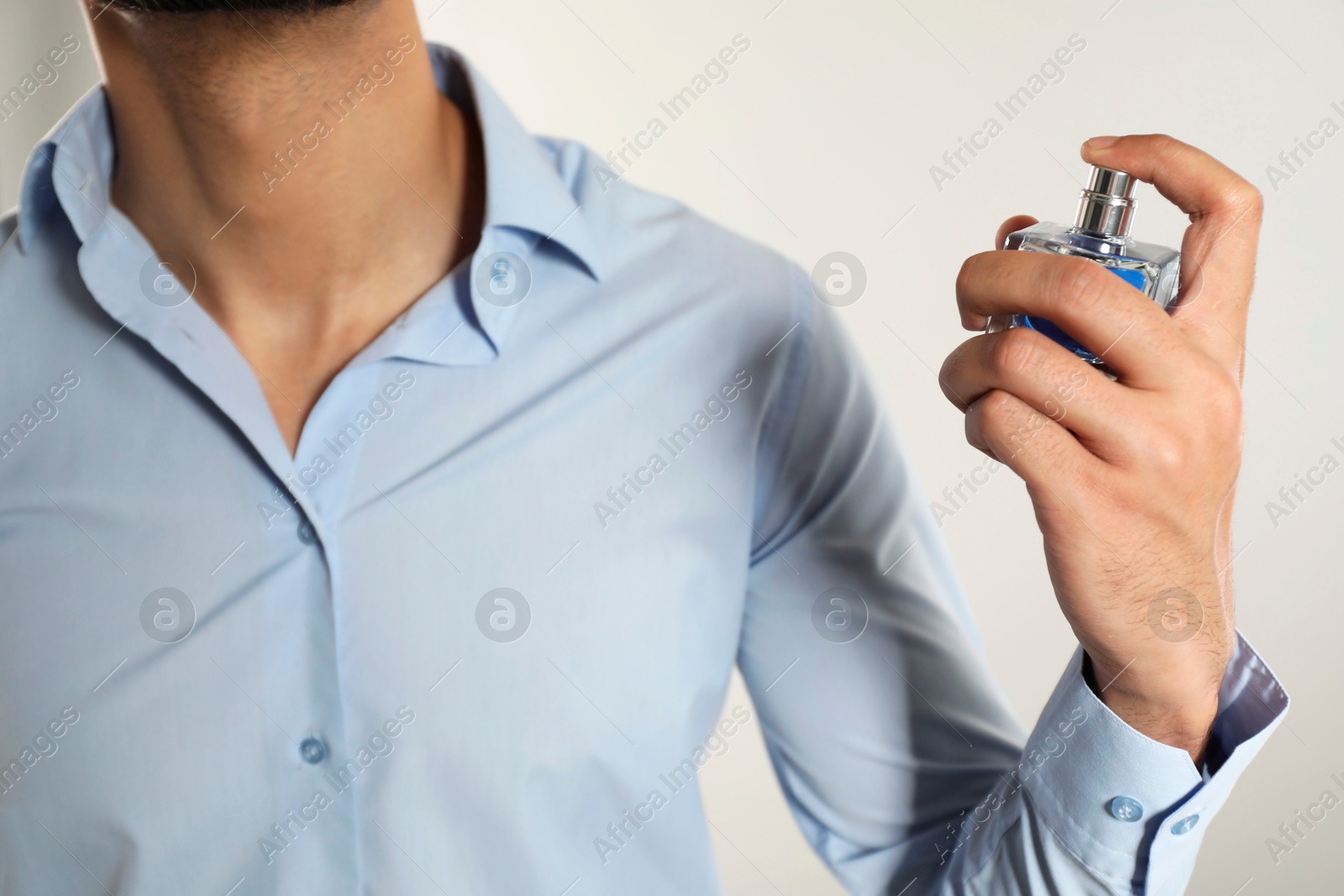 Photo of Man spraying luxury perfume on light background, closeup