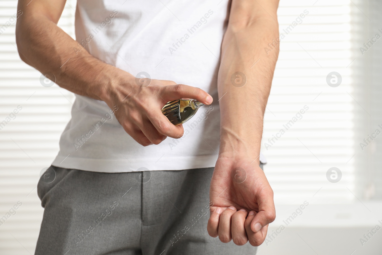 Photo of Young man spraying luxury perfume indoors, closeup