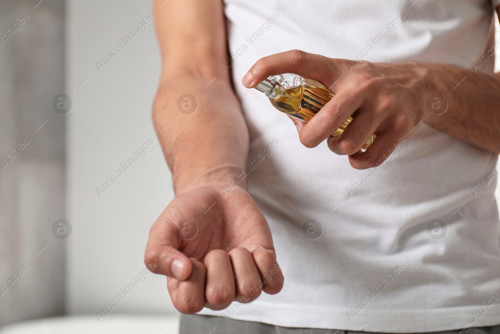 Photo of Young man spraying luxury perfume indoors, closeup