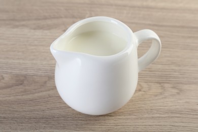 Jug of fresh milk isolated on wooden table, closeup