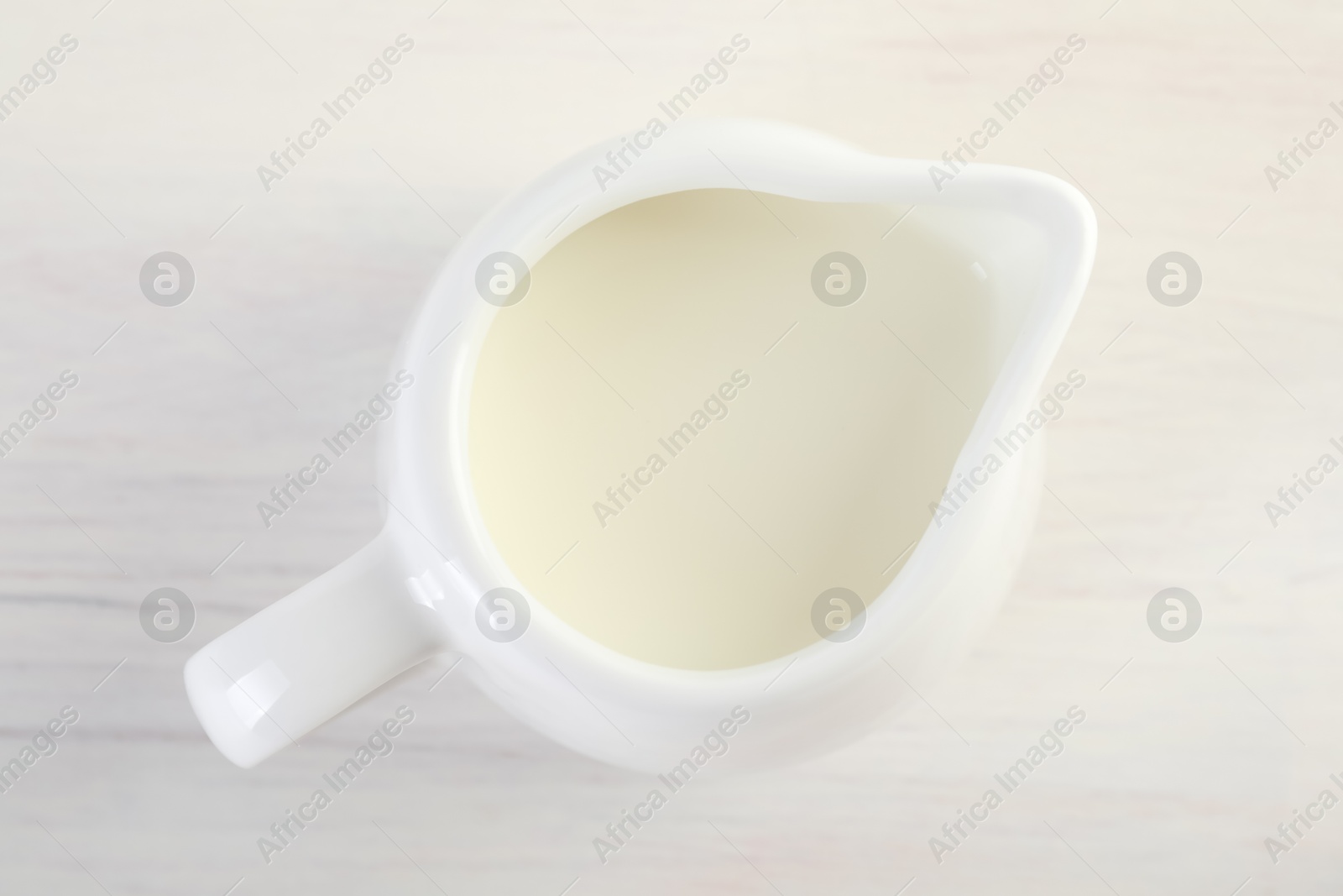 Photo of Jug of fresh milk isolated on wooden table, top view