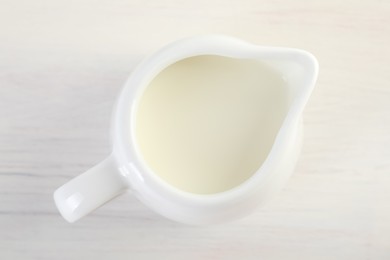 Jug of fresh milk isolated on wooden table, top view