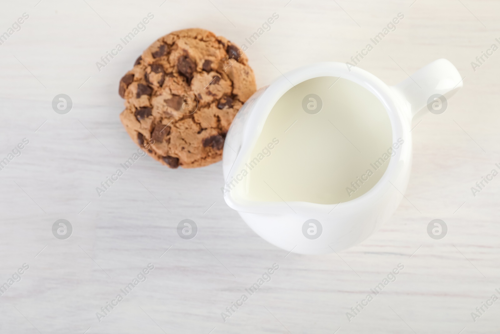 Photo of Jug of fresh milk and cookie isolated on wooden table, above view. Space for text