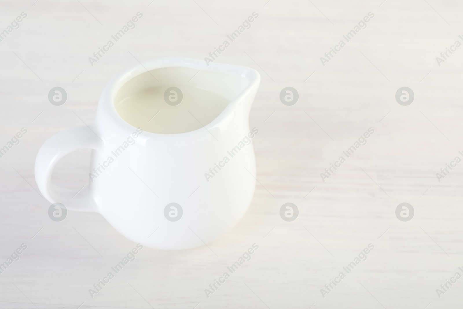 Photo of Jug of fresh milk isolated on wooden table, space for text