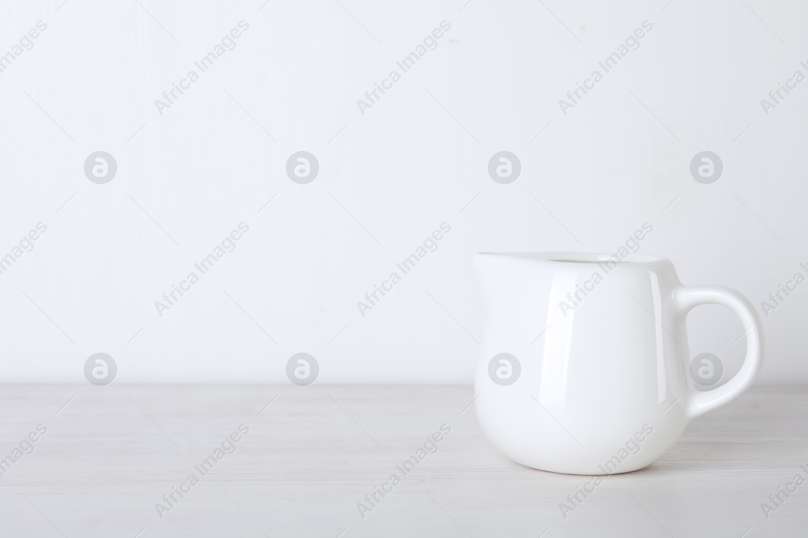 Photo of Jug of fresh milk isolated on wooden table, space for text