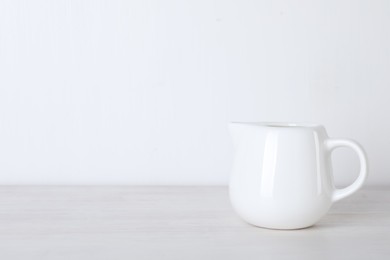 Photo of Jug of fresh milk isolated on wooden table, space for text