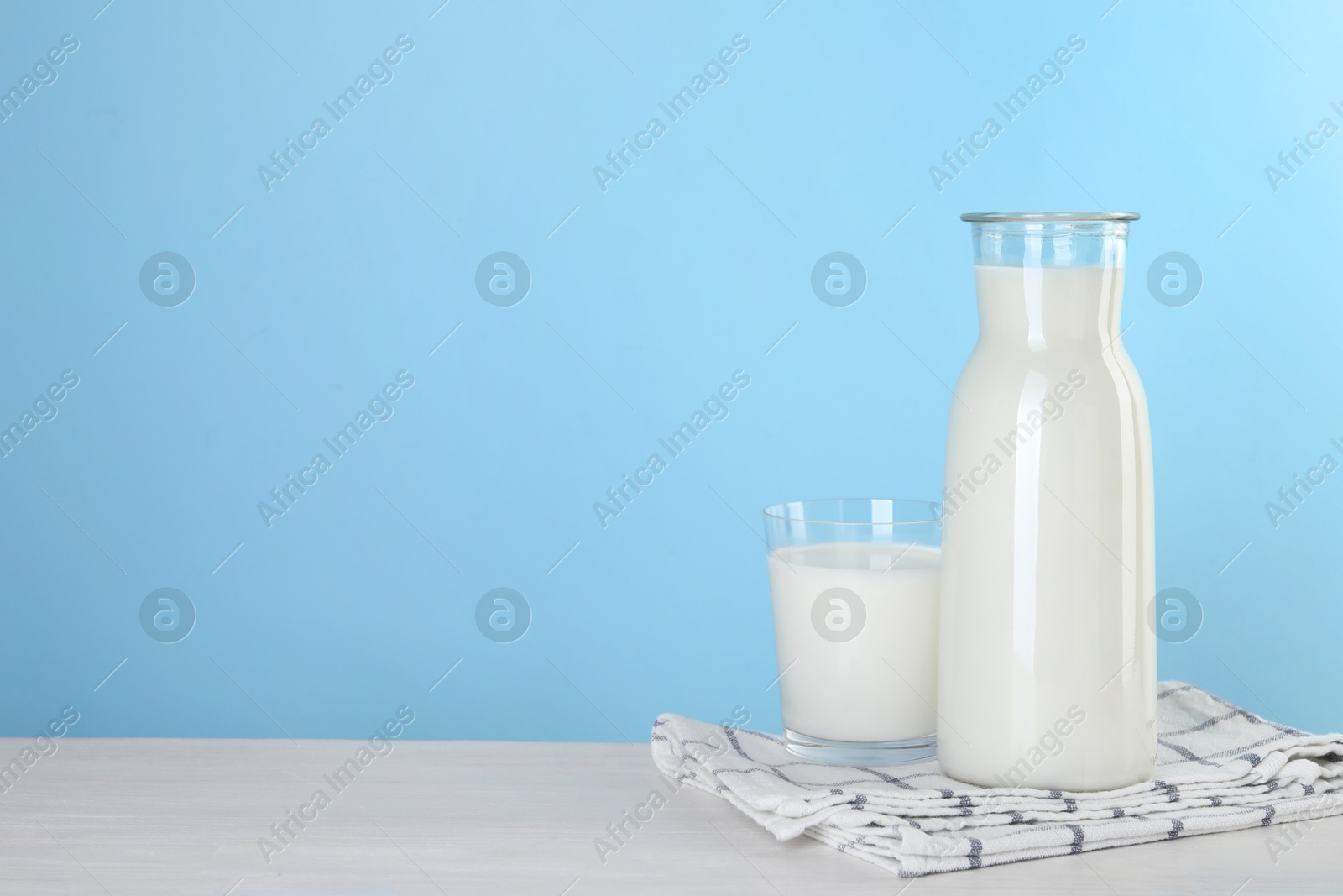 Photo of Carafe and glass of fresh milk on table against light blue background, space for text