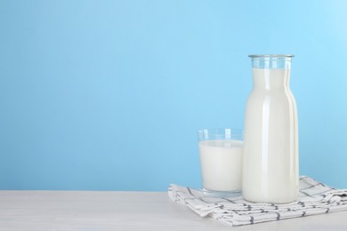 Photo of Carafe and glass of fresh milk on table against light blue background, space for text