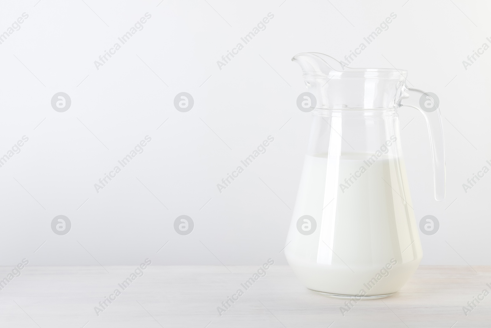 Photo of Jug of fresh milk on wooden table, space for text