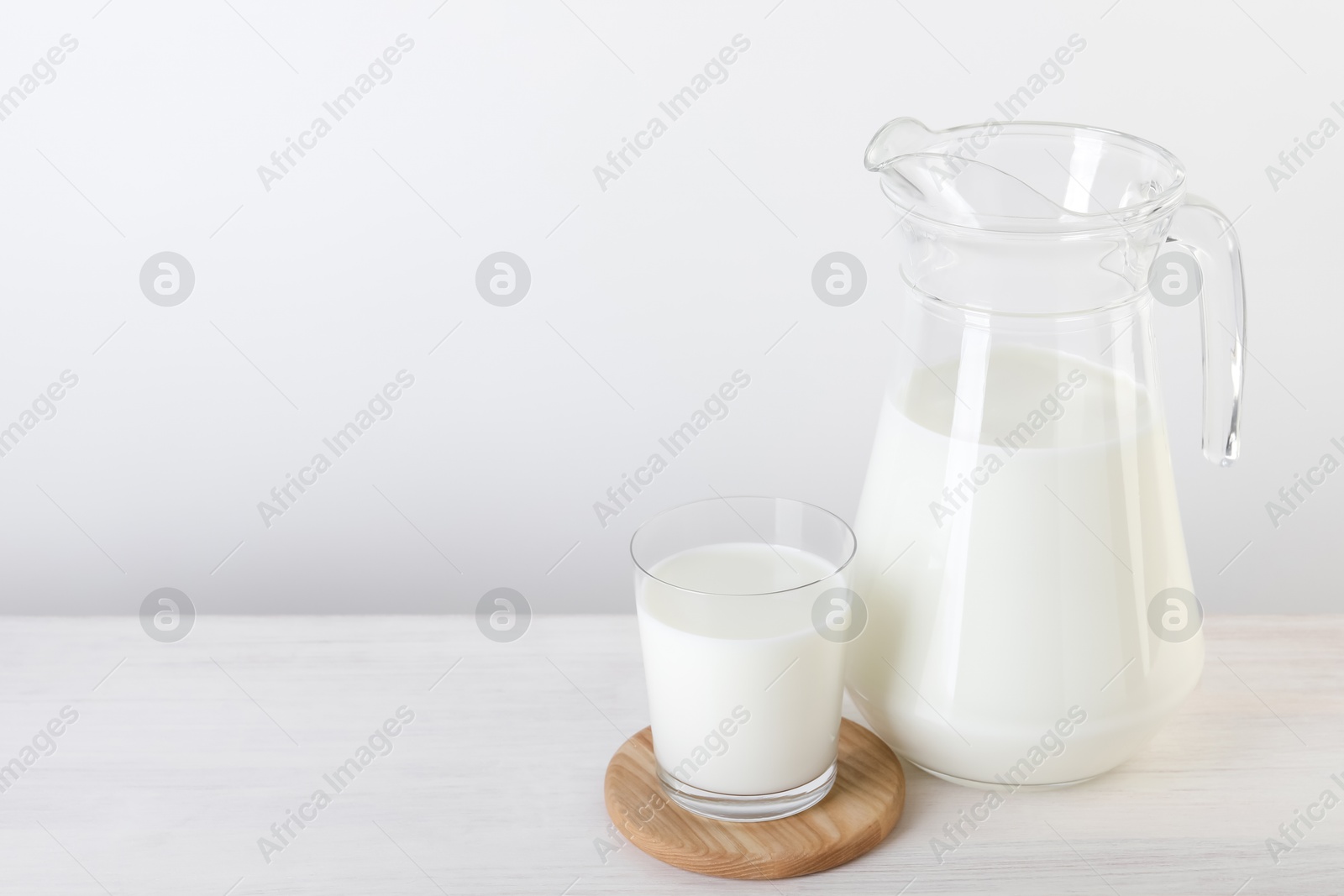 Photo of Jug and glass of fresh milk on wooden table, space for text