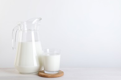 Photo of Jug and glass of fresh milk on wooden table, space for text