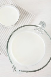 Jug and glass of fresh milk on wooden table, top view