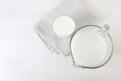 Jug and glass of fresh milk on wooden table, top view. Space for text