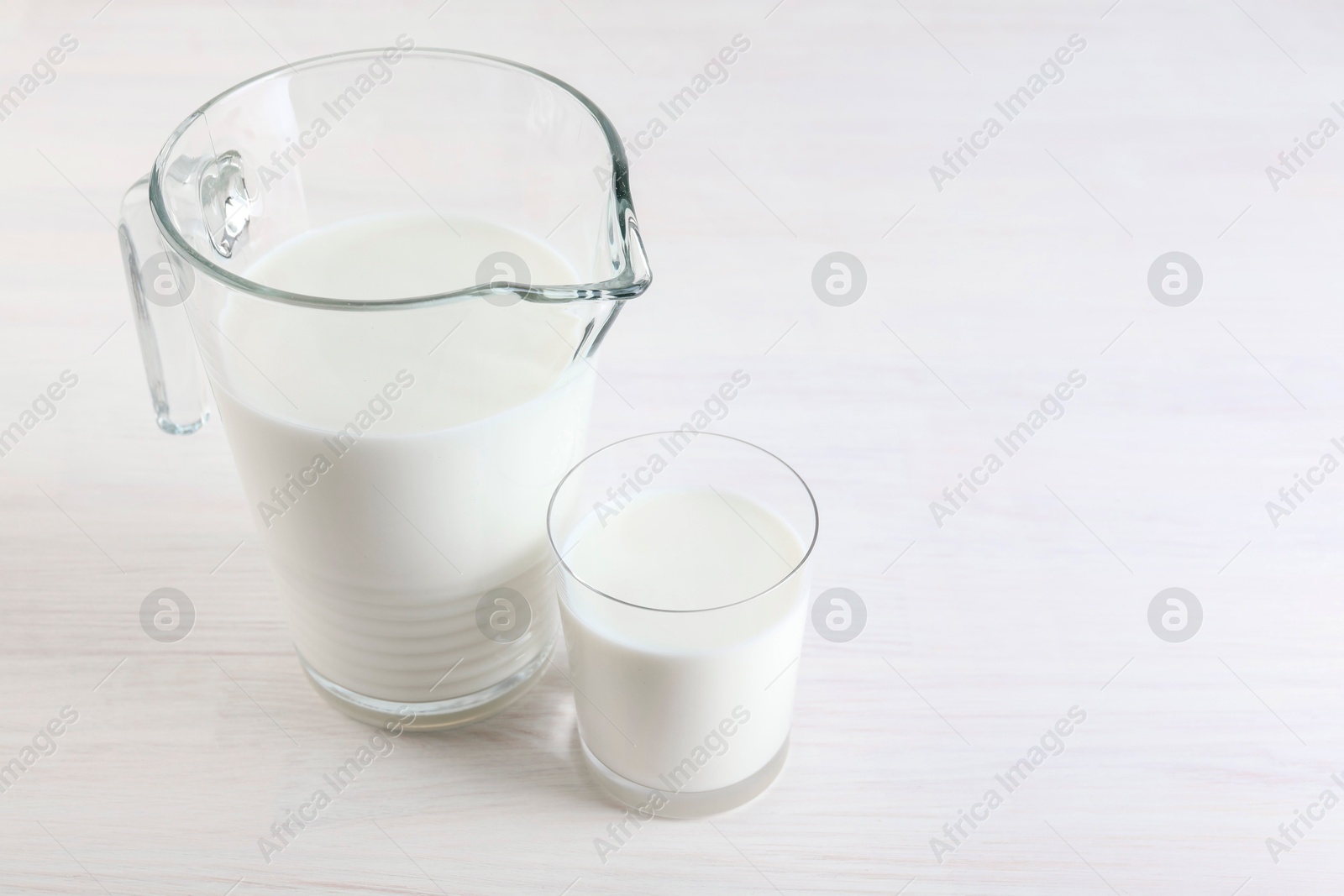 Photo of Jug and glass of fresh milk on wooden table, space for text