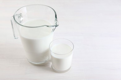 Jug and glass of fresh milk on wooden table, space for text