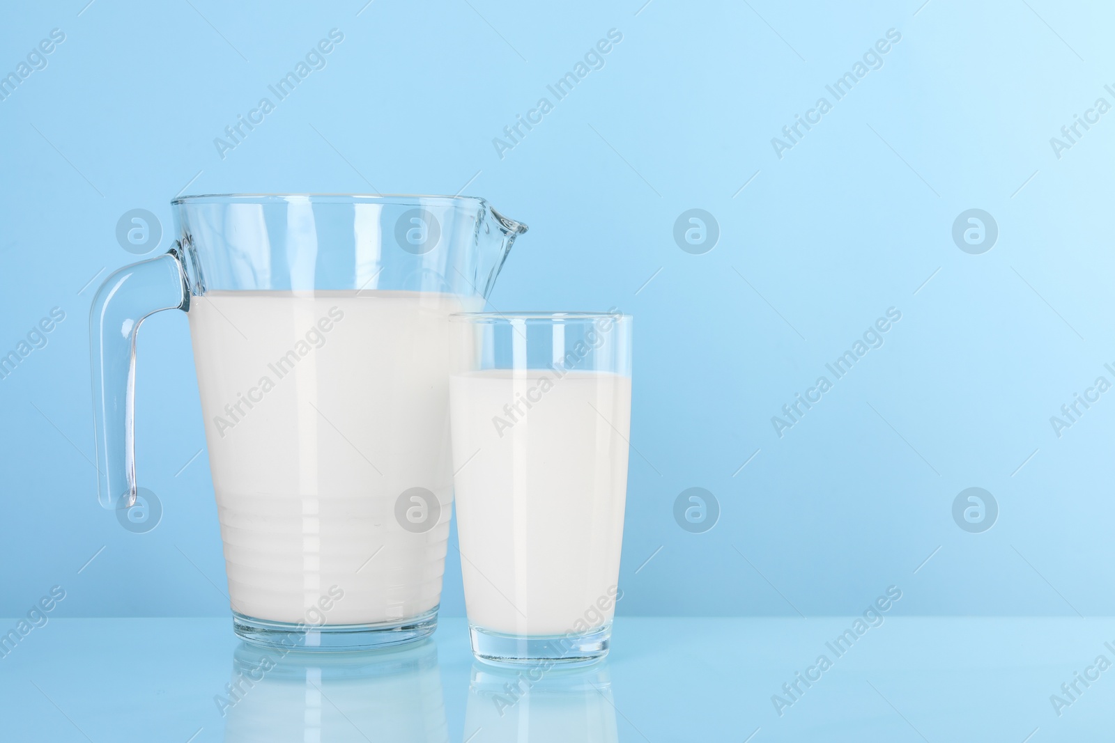 Photo of Jug and glass of fresh milk on light blue background, space for text