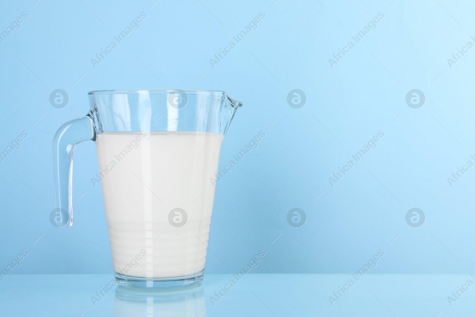 Photo of Jug of fresh milk on light blue background, space for text