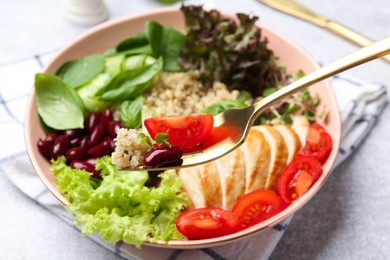 Photo of Healthy meal. Eating tasty vegetables, quinoa and chicken breast with fork from bowl on white table, closeup