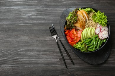 Photo of Healthy meal. Tasty products in bowl and cutlery on black wooden table, top view. Space for text