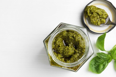 Tasty pesto sauce in jar, spoon and basil on white wooden table, top view. Space for text