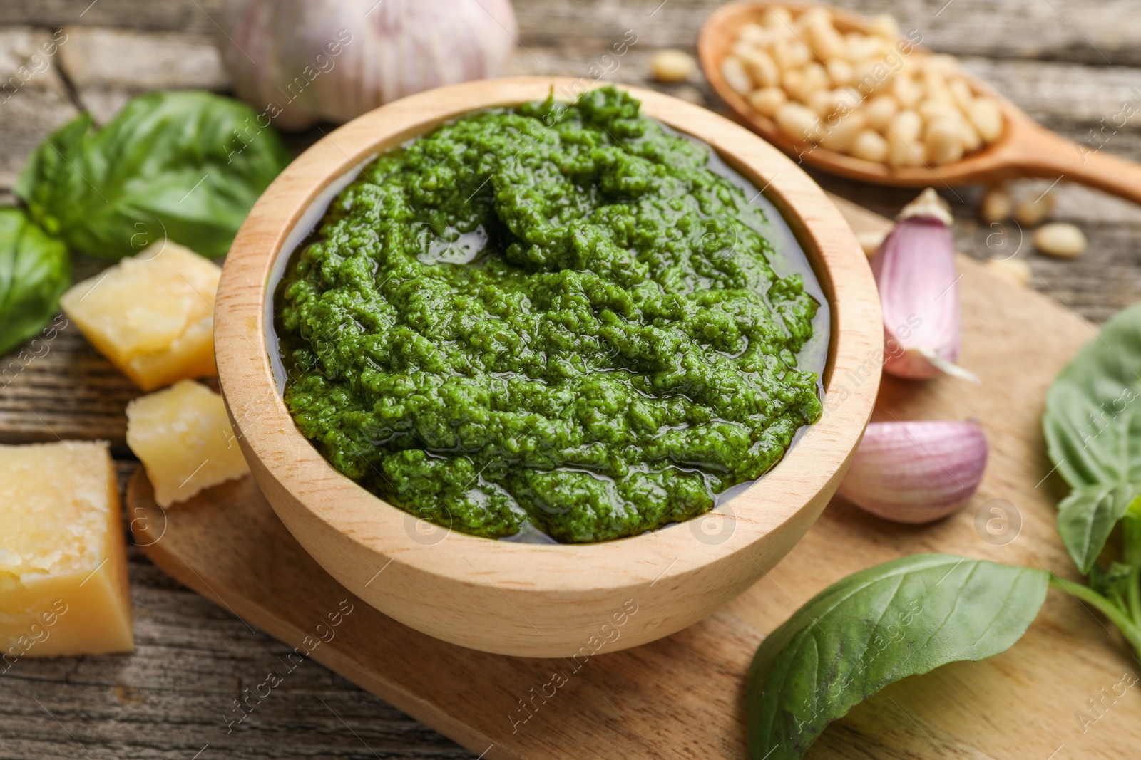 Photo of Tasty pesto sauce in bowl, basil, pine nuts, cheese and garlic on wooden table, closeup