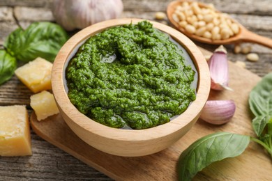 Photo of Tasty pesto sauce in bowl, basil, pine nuts, cheese and garlic on wooden table, closeup