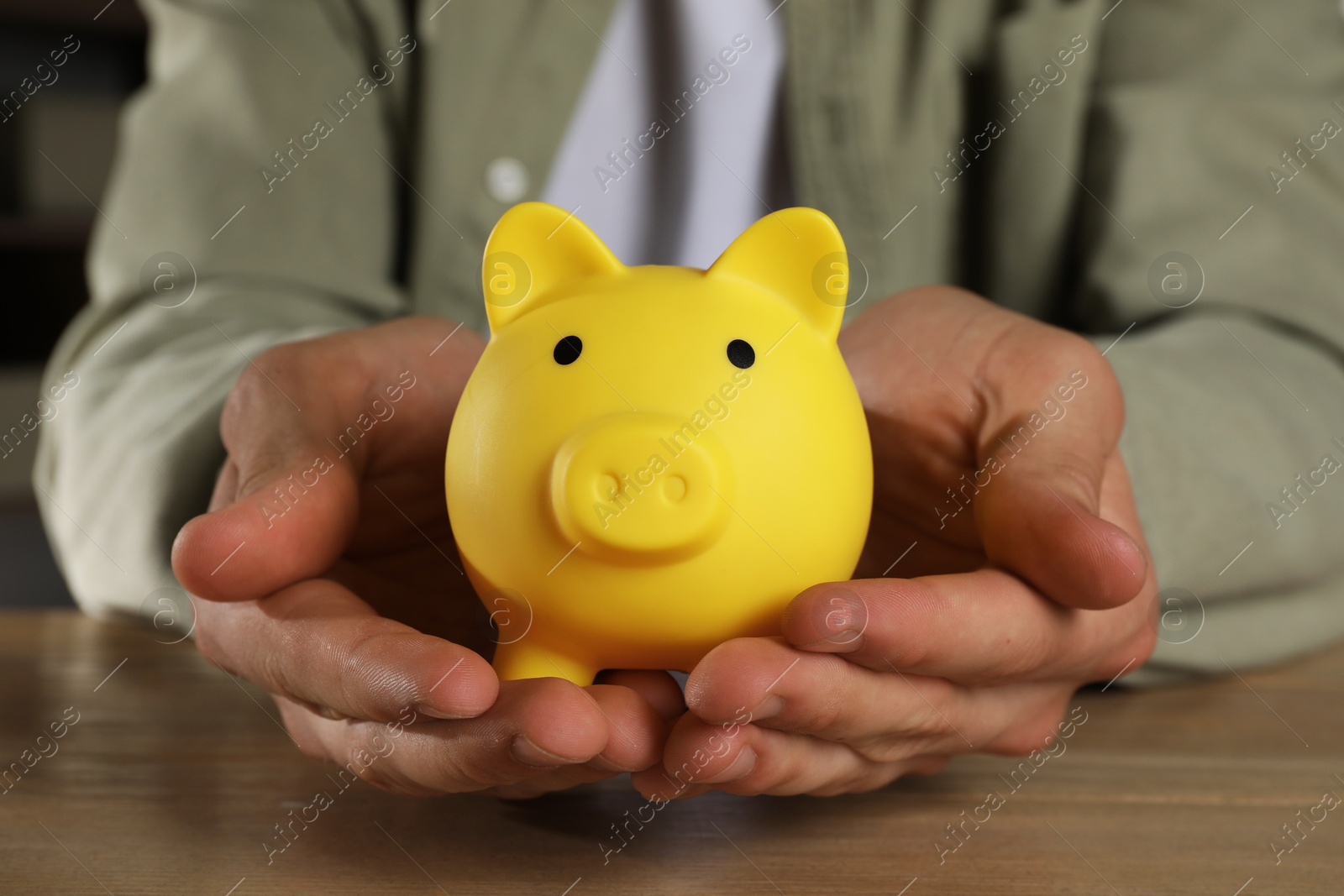 Photo of Man with yellow piggy bank on wooden table, closeup