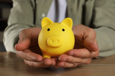 Photo of Man with yellow piggy bank on wooden table, closeup