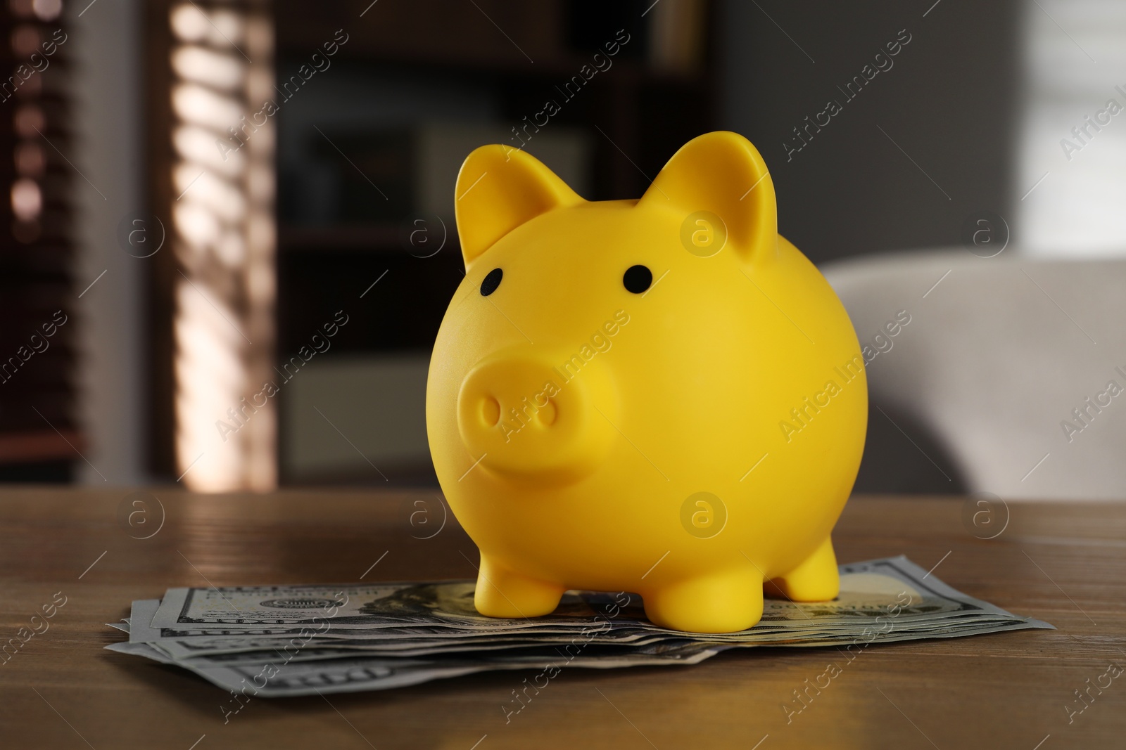 Photo of Yellow piggy bank and banknotes on wooden table