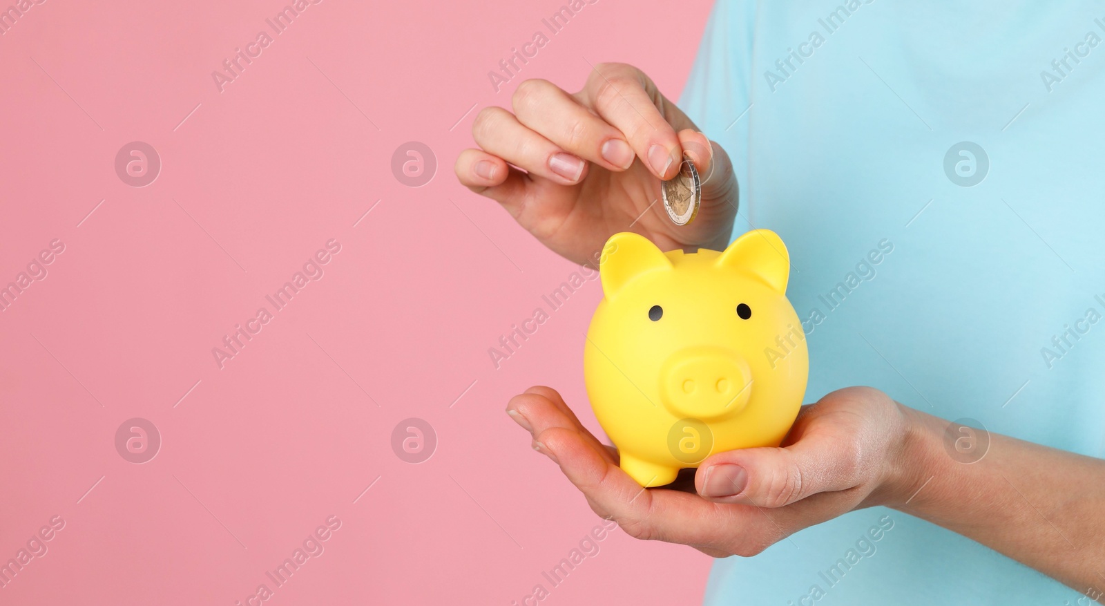 Photo of Woman putting coin into yellow piggy bank on pink background, closeup. Space for text