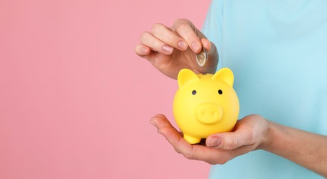 Photo of Woman putting coin into yellow piggy bank on pink background, closeup. Space for text