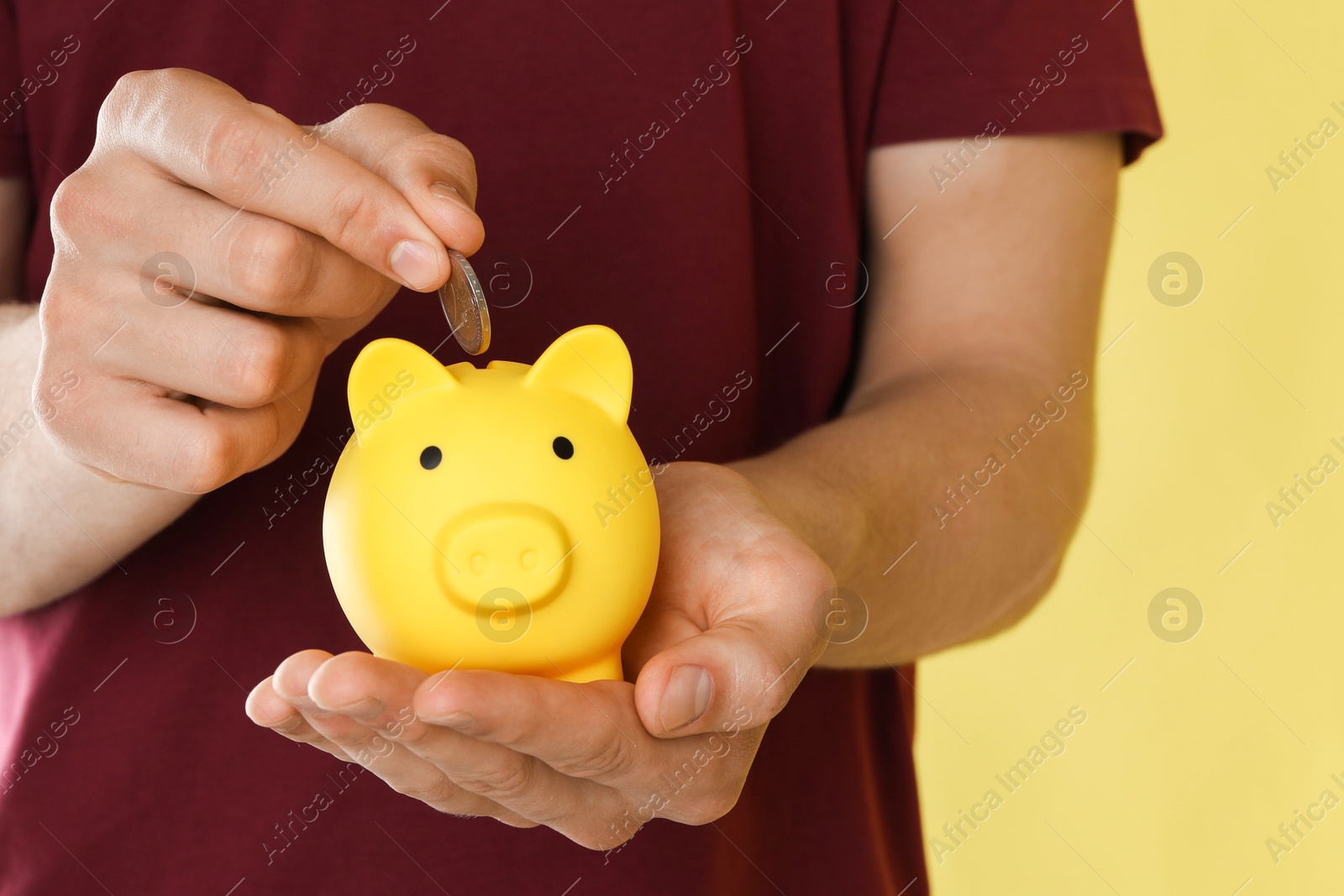 Photo of Man putting coin into piggy bank on yellow background, closeup. Space for text