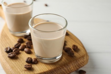 Coffee cream liqueur in glasses and beans on white wooden table, closeup
