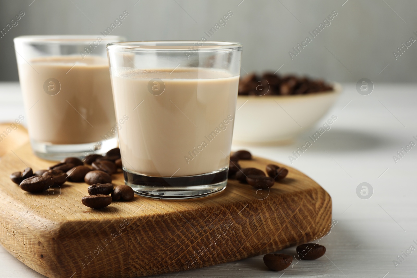 Photo of Coffee cream liqueur in glasses and beans on white wooden table, closeup