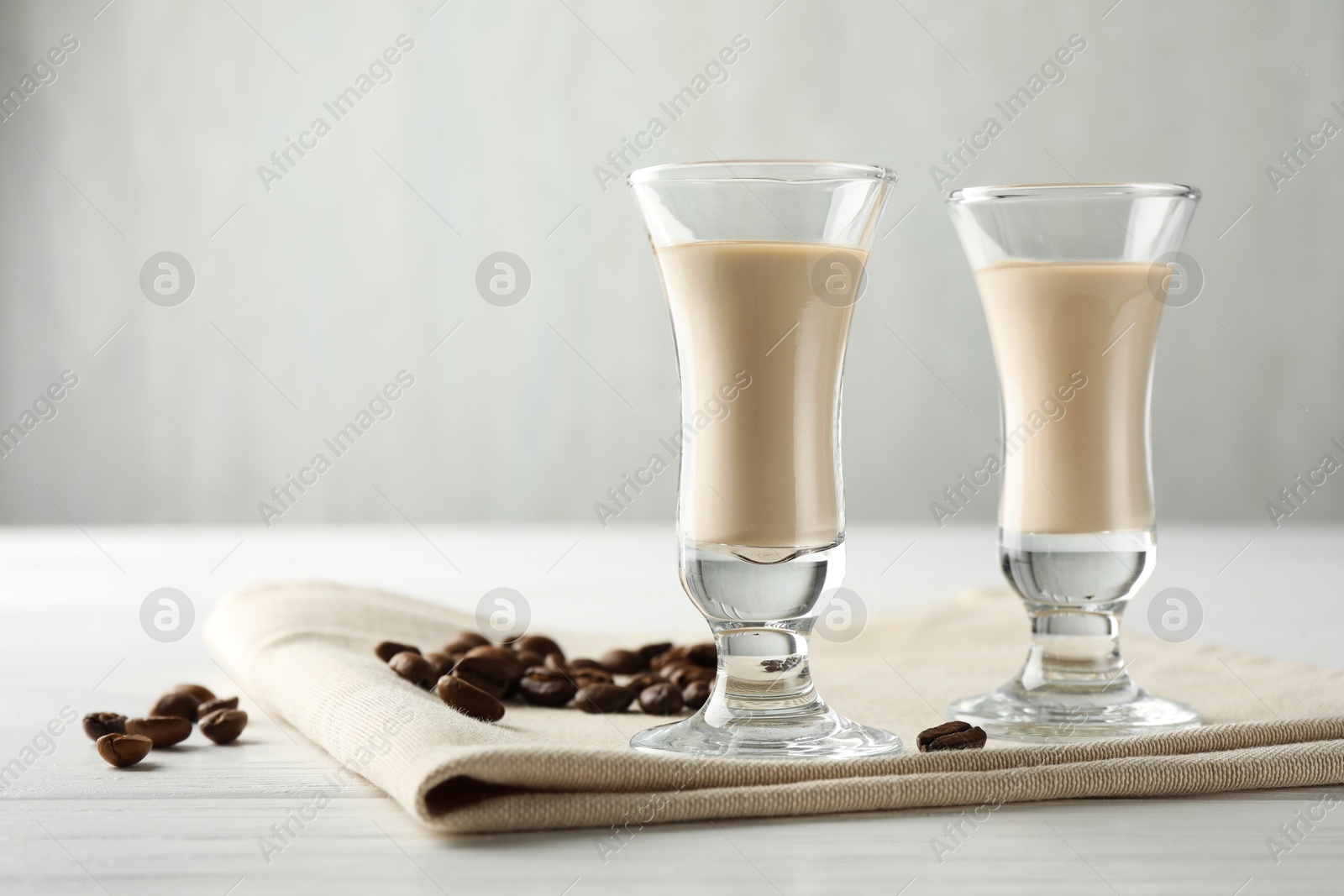 Photo of Coffee cream liqueur in glasses and beans on white wooden table