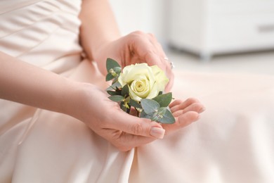 Bride holding boutonniere for her groom indoors, closeup