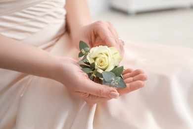 Bride holding boutonniere for her groom indoors, closeup