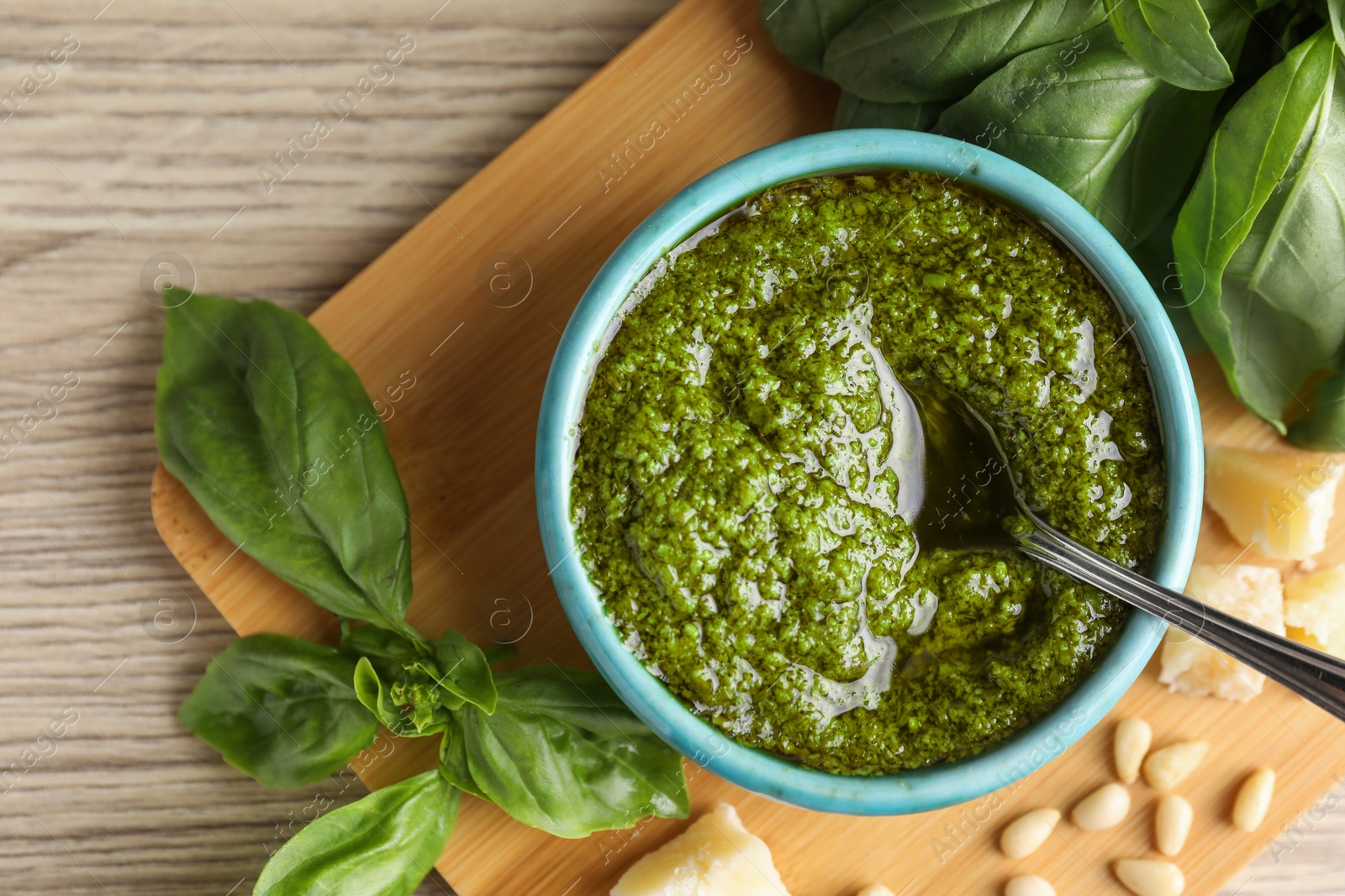 Photo of Tasty pesto sauce in bowl, basil, pine nuts and cheese on wooden table, top view