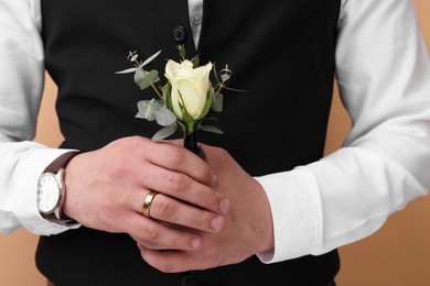 Groom with boutonniere on beige background, closeup. Wedding accessory