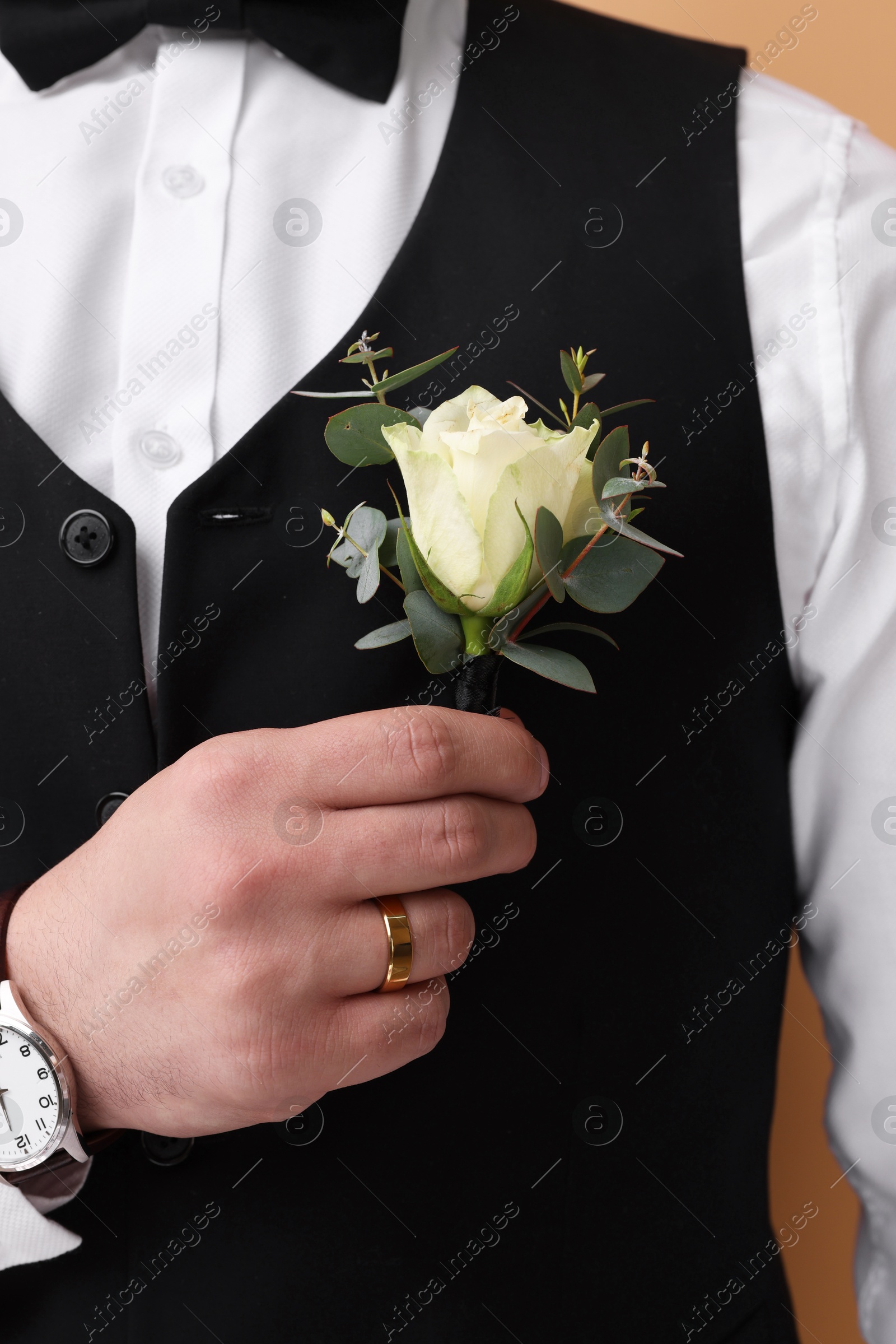 Photo of Handsome young groom with boutonniere on beige background. Wedding accessory