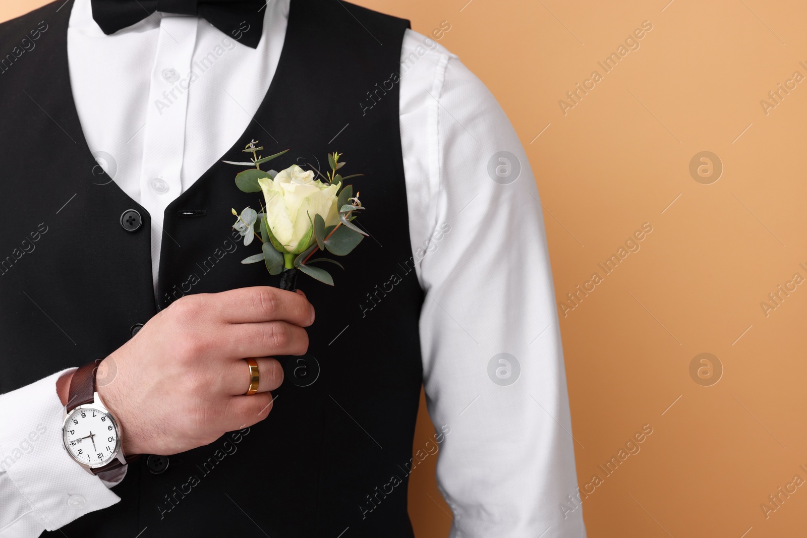 Photo of Handsome young groom with boutonniere on beige background. Wedding accessory